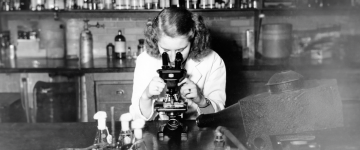 A black and white photo of a woman looking into a microscope in 1948